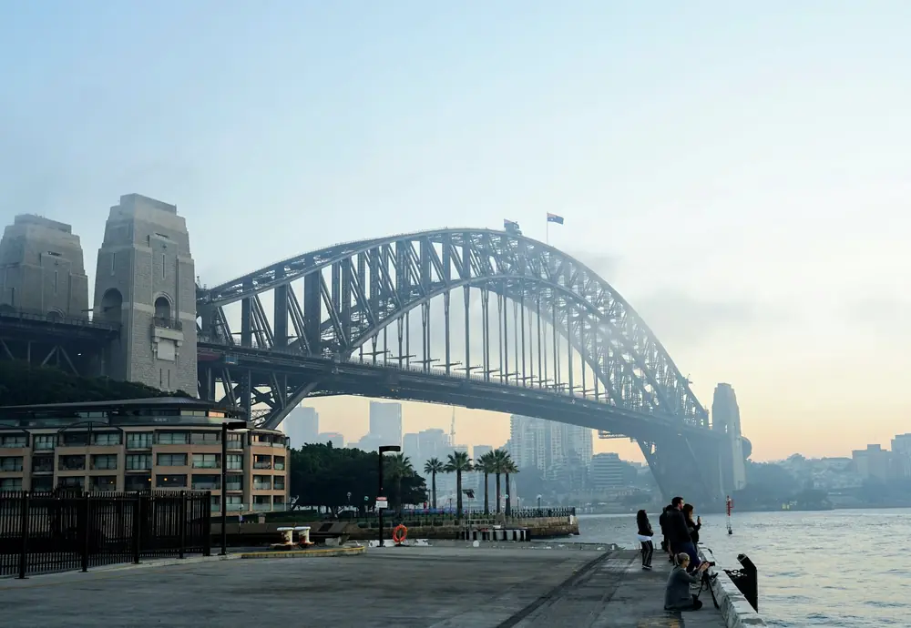 清晨的悉尼港，海港大桥下有人沿着水边散步